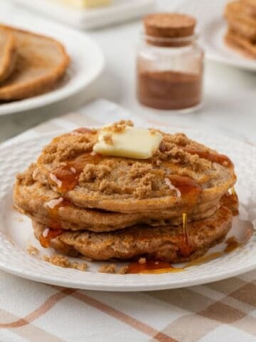 stack of cinnamon pancakes on a plate topped with a little butter, brown sugar, and pancake syrup