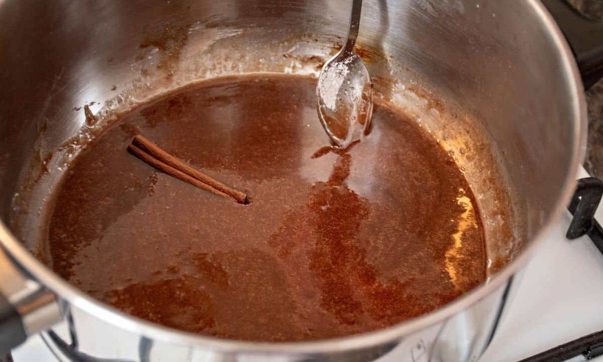 maple syrup, cinnamon, and a cinnamon stick simmering in a pot with a spoon stirring