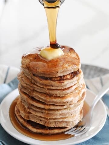 front view of cinnamon syrup being poured over a stack of pancakes