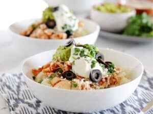 two white bowls filled with cauilflower rice, chicken, shredded cheese, guacamole, sour cream and sliced olives