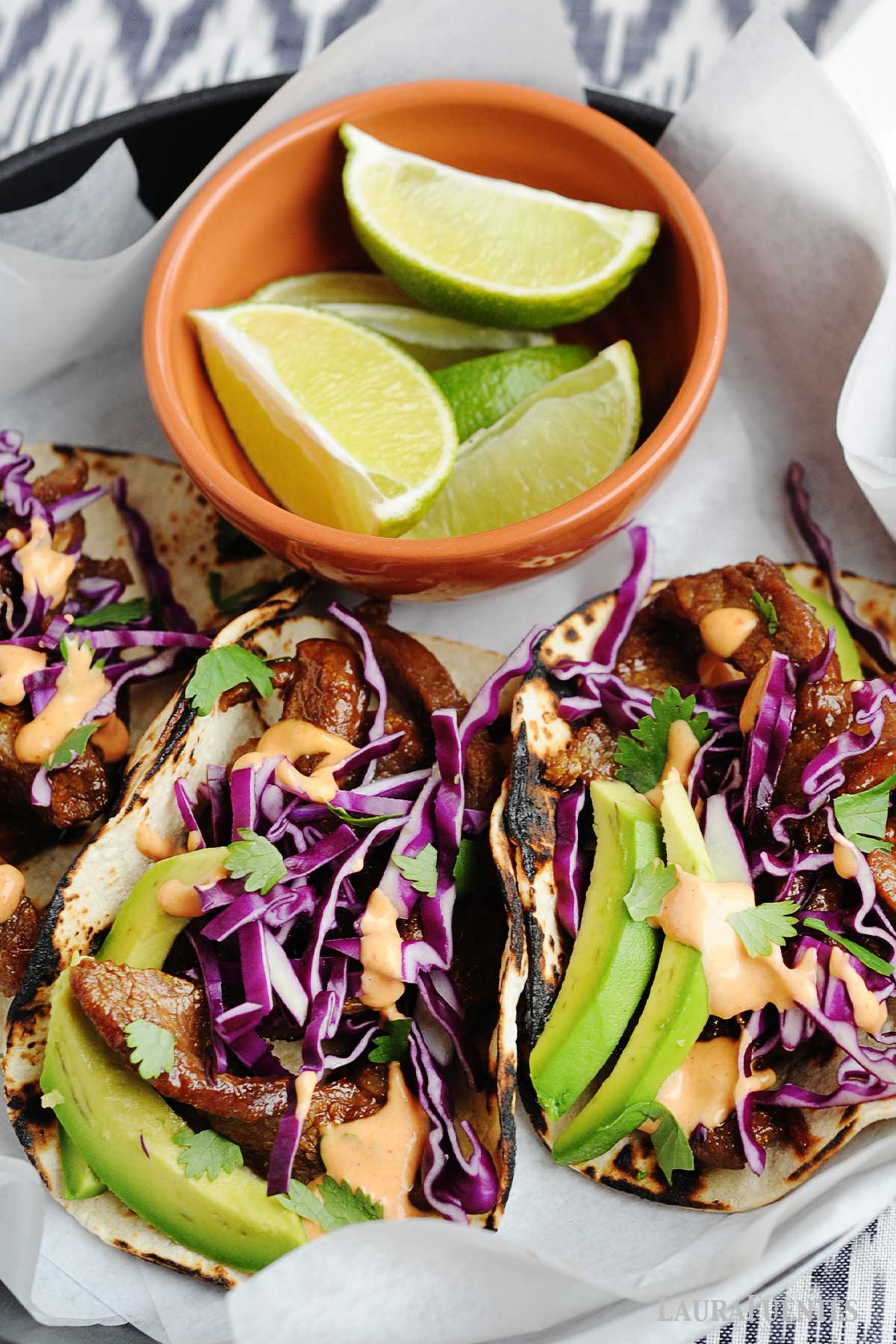 beef tacos with red cabbage and avocado slices, and a small orange bowl of lime wedges