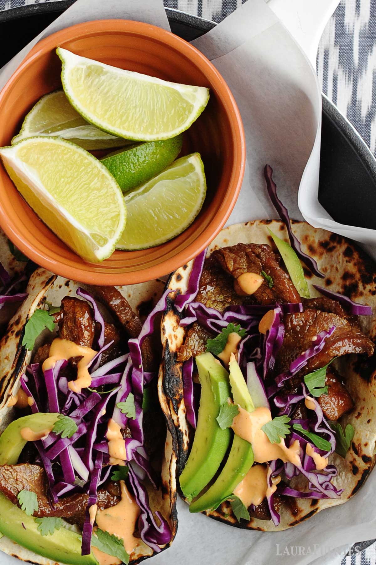 beef tacos with red cabbage and avocado slices, and a small orange bowl of lime wedges