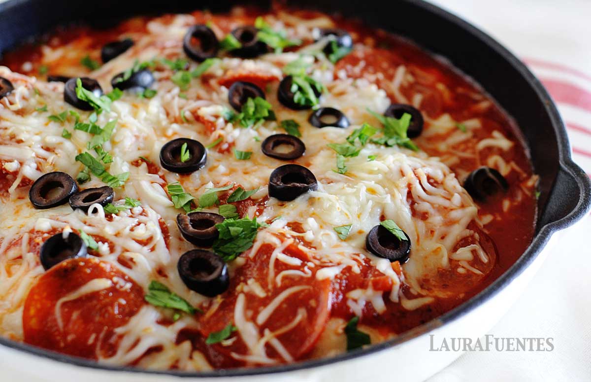 image: white skillet with chicken, red sauce, pepperonis, sliced olives and grated cheese