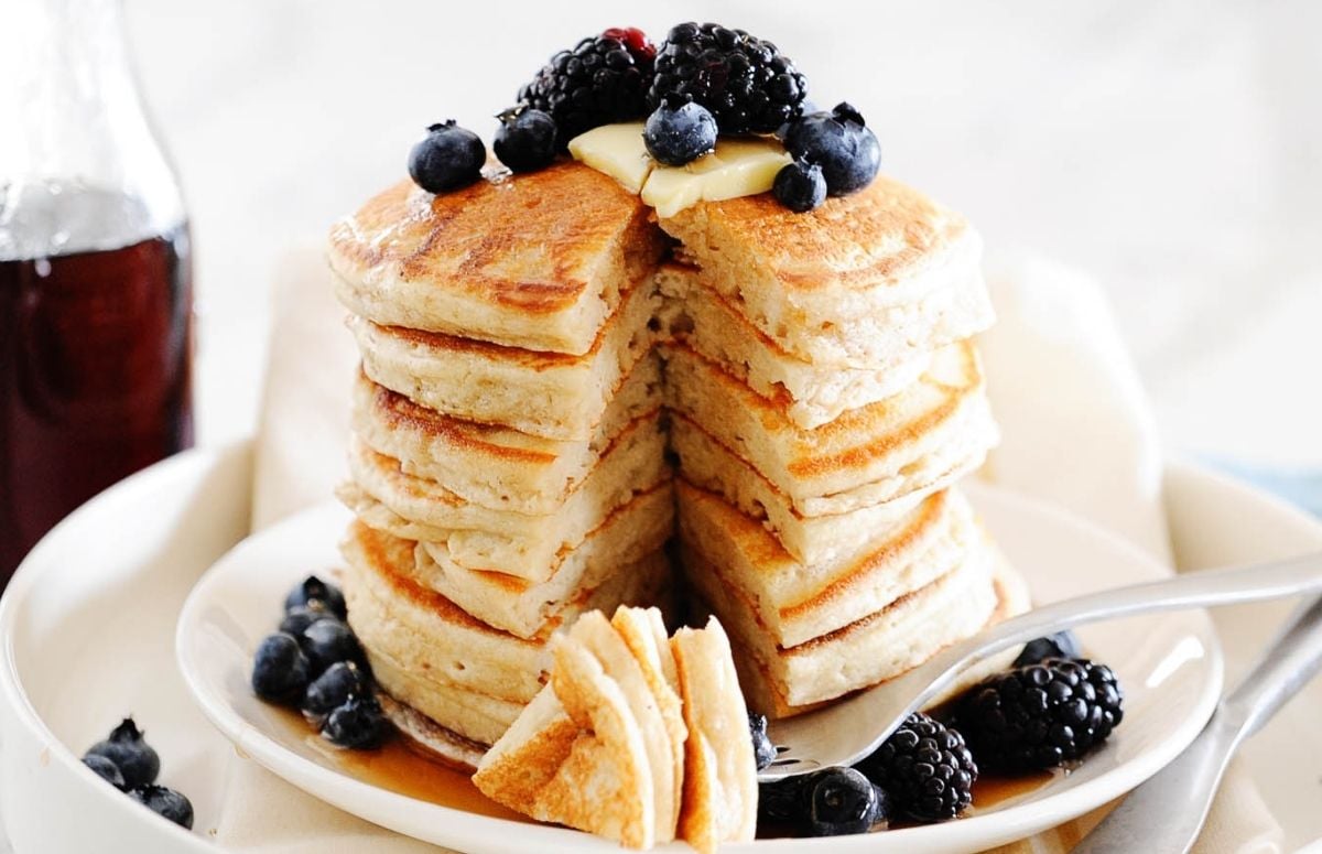stack of fluffy cassava flour pancakes on a plate with a slice cut. topped with blueberries and butter and syrup