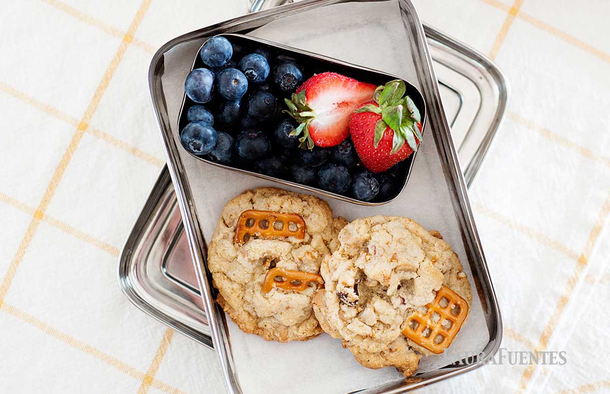 kitchen sink cookies in a metal food container with strawberries and blueberries on the side