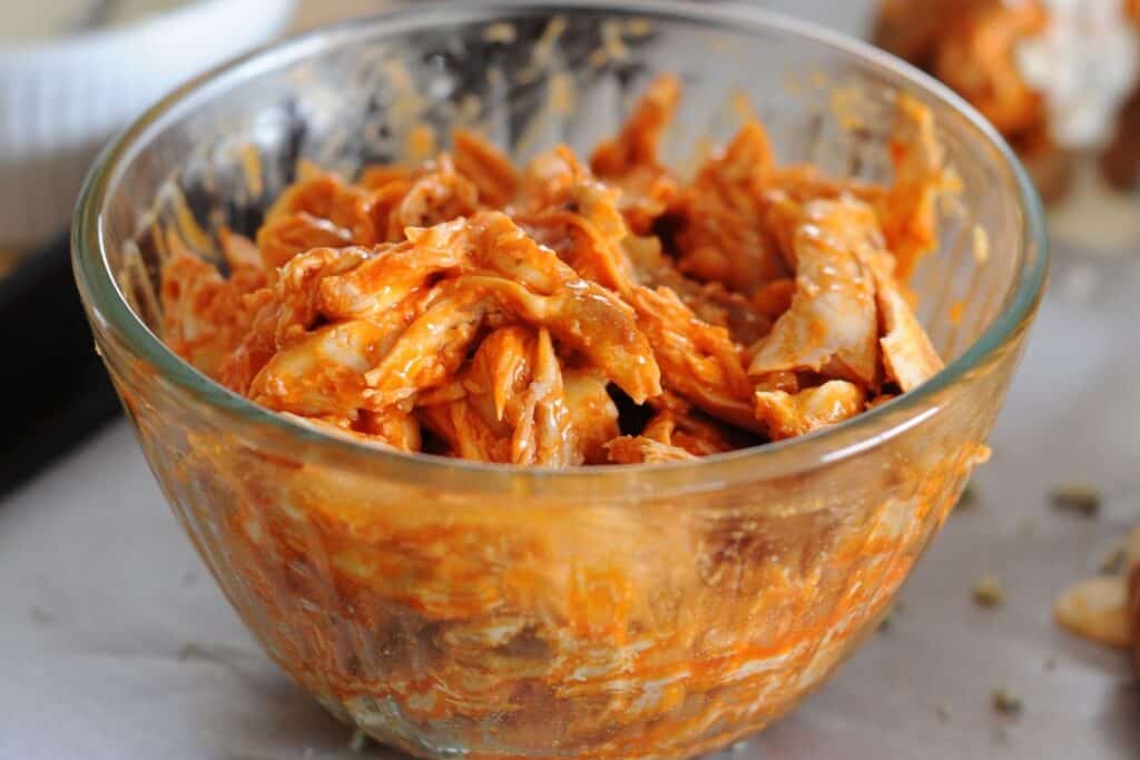 large glass bowl of shredded chicken with buffalo sauce