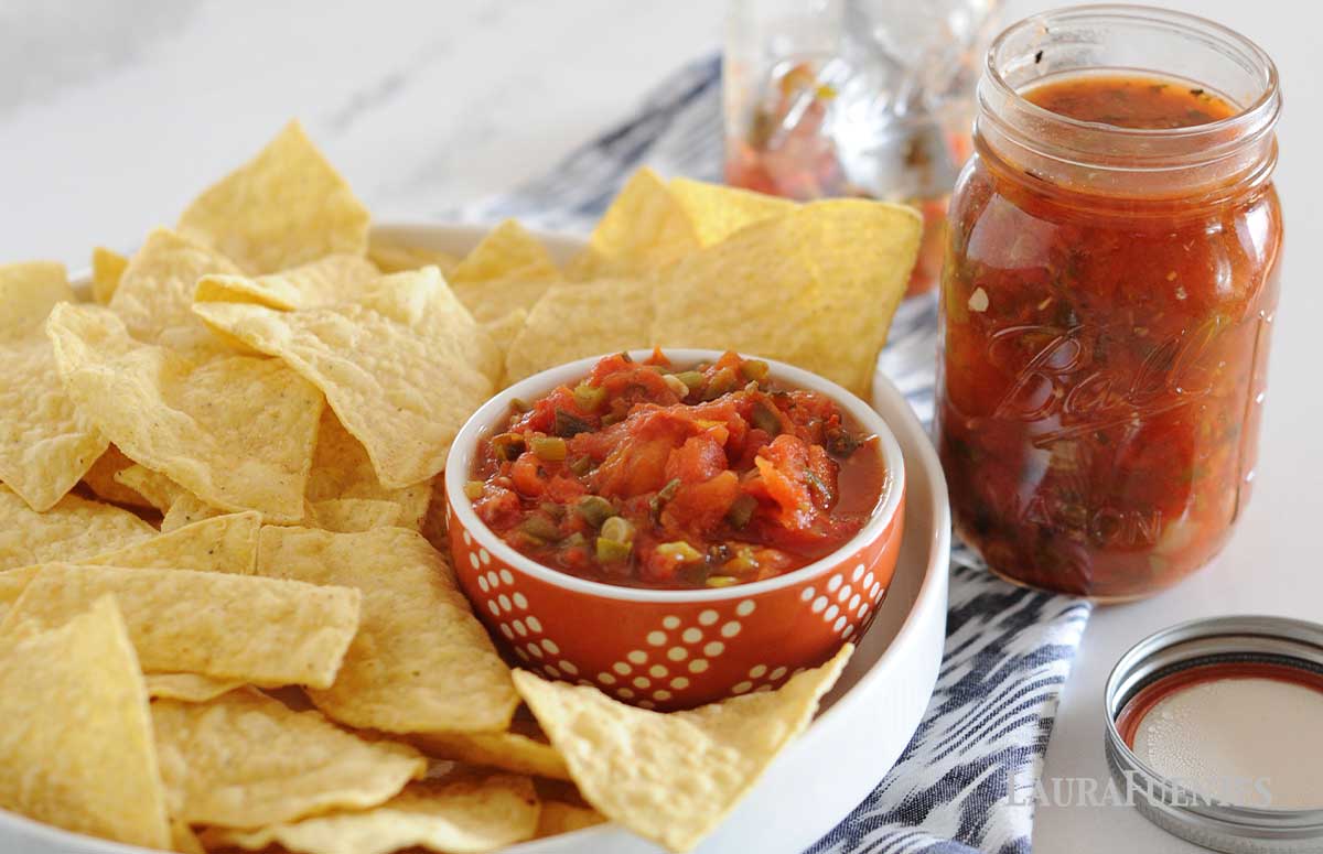image: can of red salsa next to tray of corn chips and bowl of red salsa