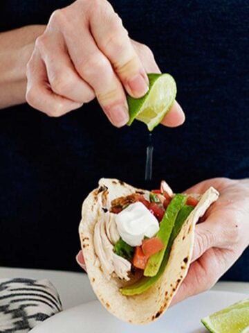 a woman squeezing lime over a mexican chicken taco