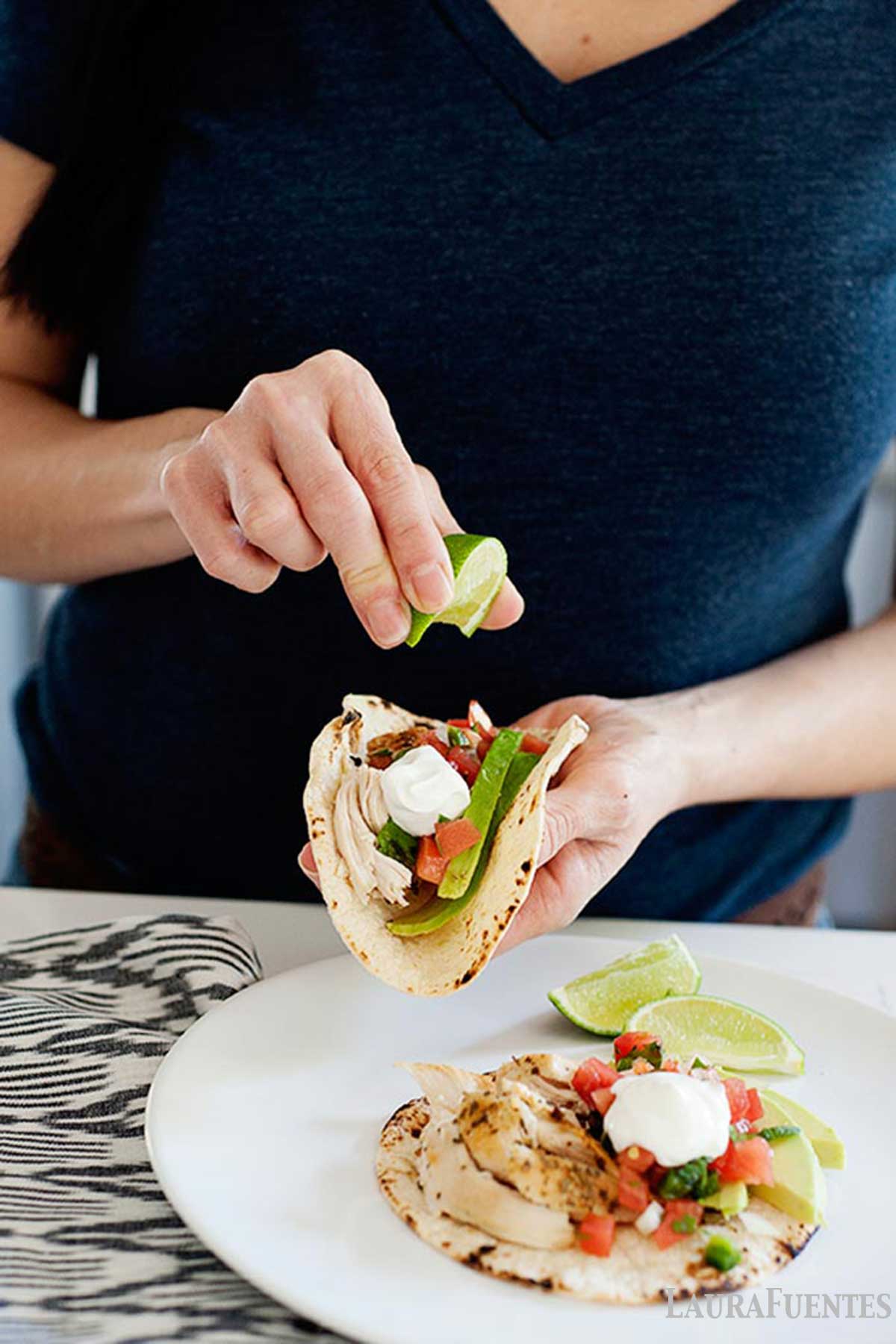 a woman squeezing lime over a mexican chicken taco