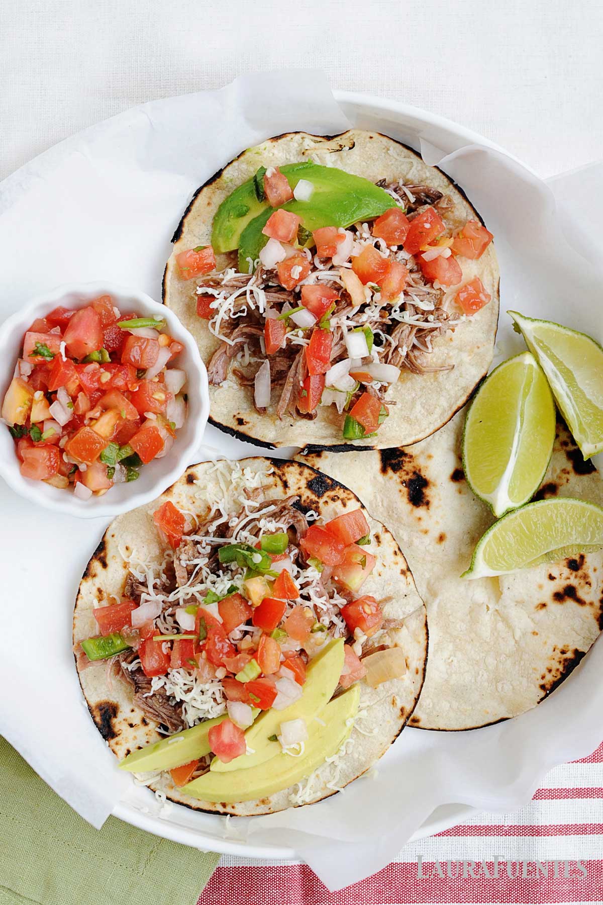 two street tacos next to a little bowl of pico de gallo and lime wedges