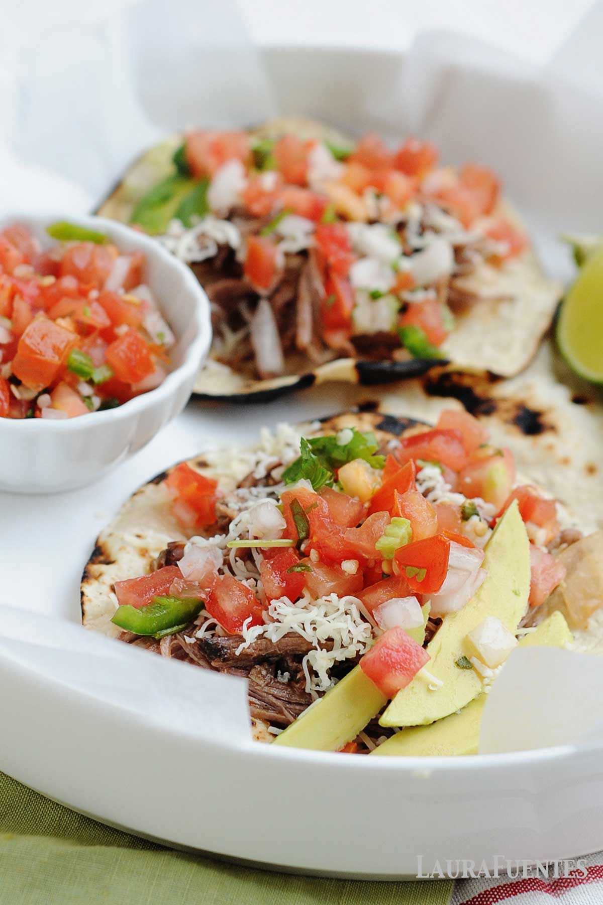 two street tacos next to a little bowl of pico de gallo and lime wedges