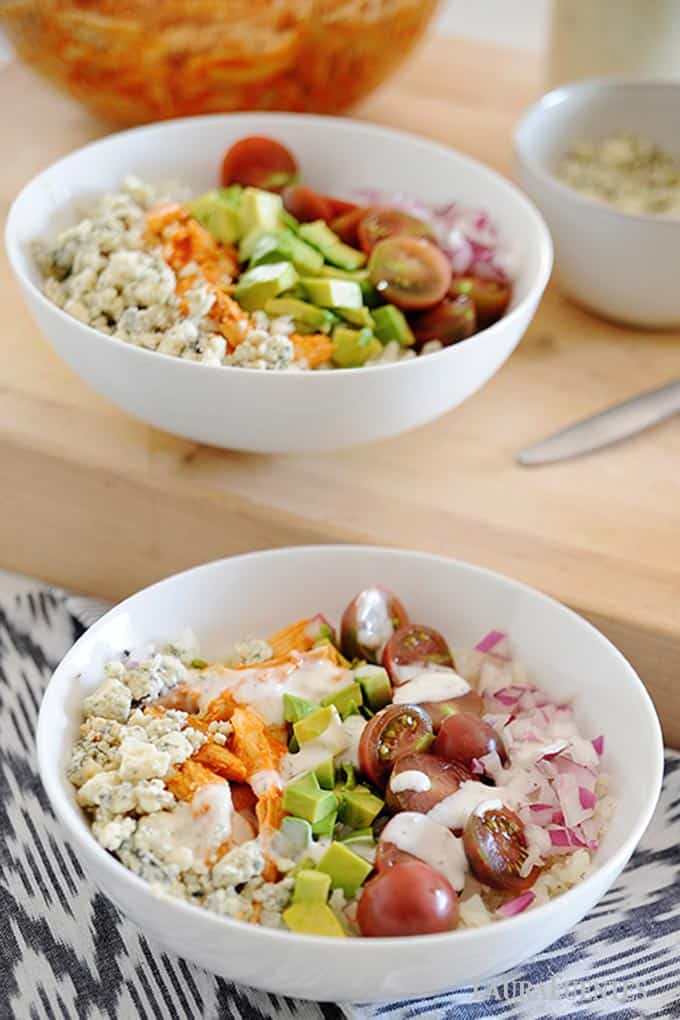 two white bowls of buffalo chicken, rice and vegetables