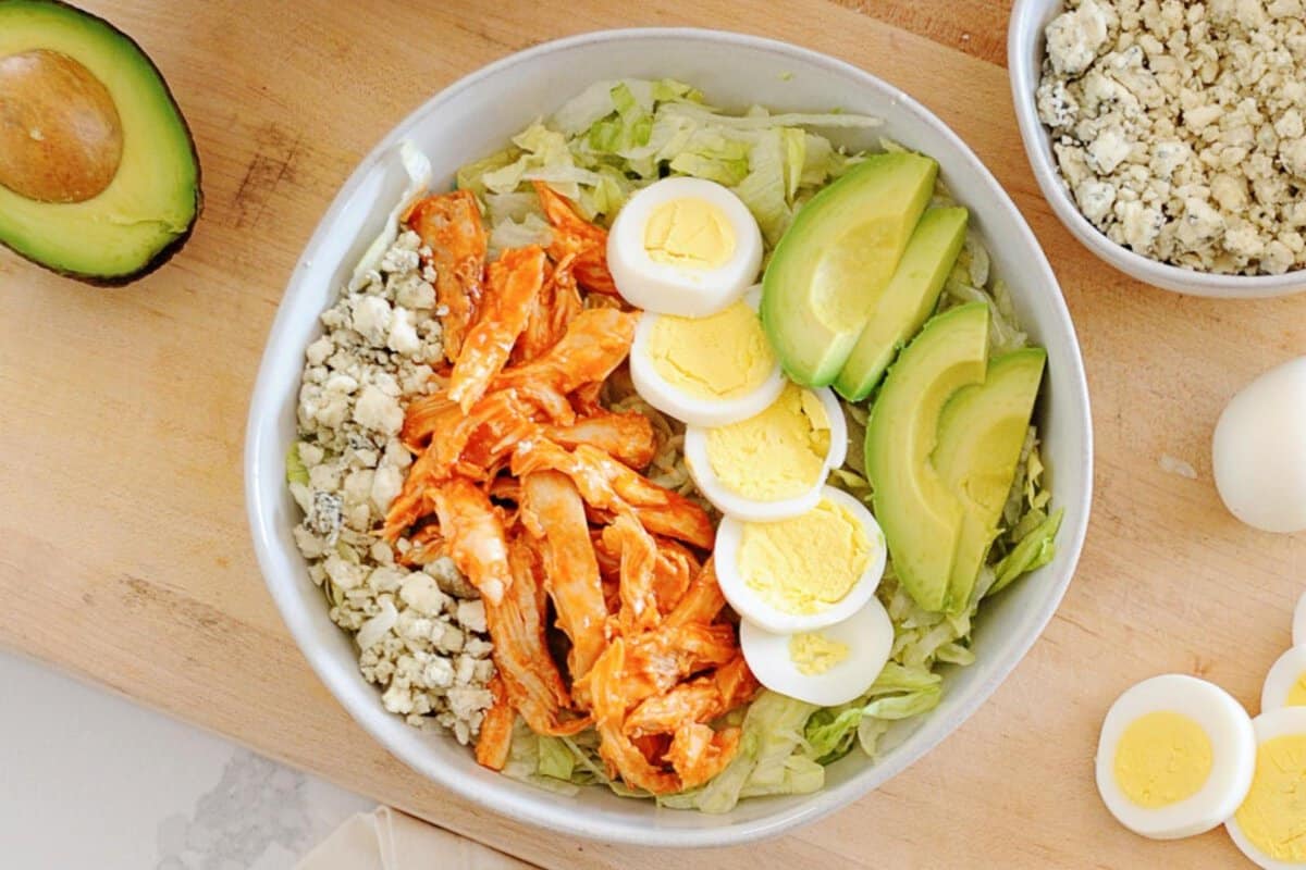 a bowl of buffalo chicken salad with hard boiled egg, avocado, and blue cheese crumbles