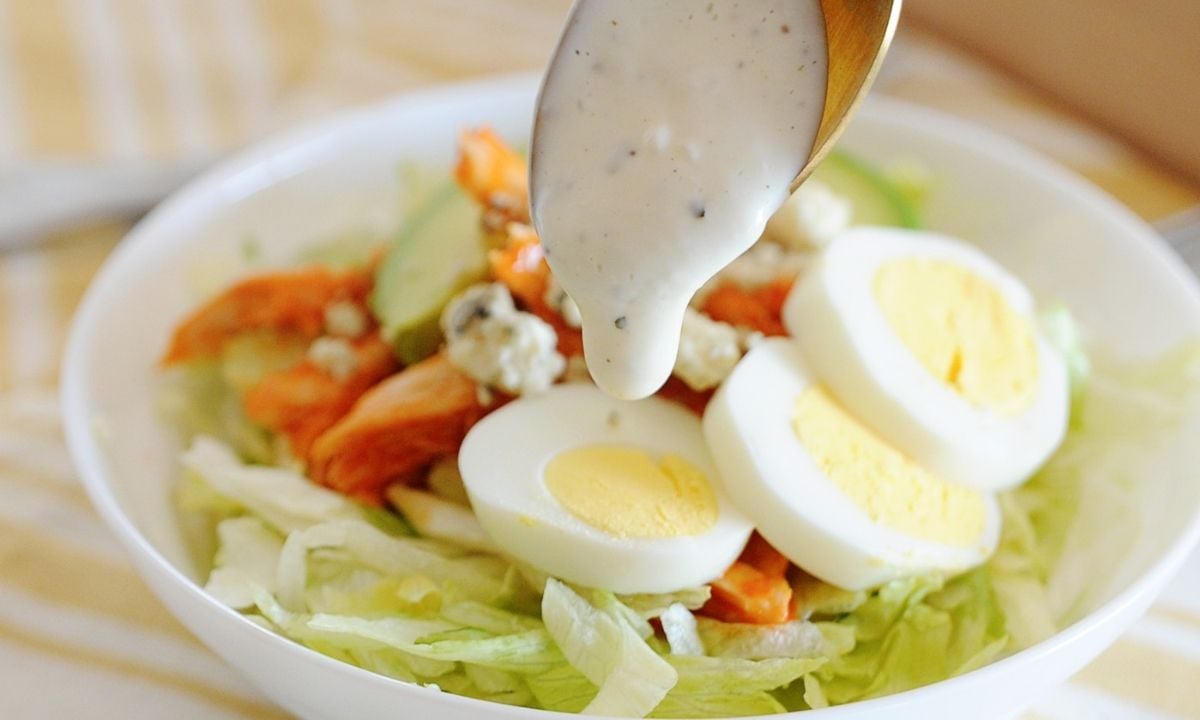 dressing being poured over a buffalo chicken salad bowl