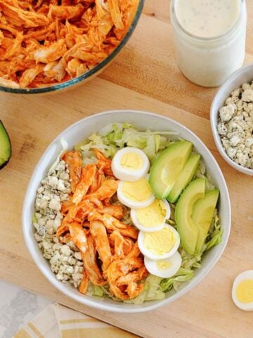 a bowl of buffalo chicken salad with hard boiled egg and avocado, next to a bowl of buffalo chicken