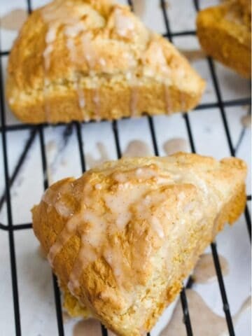 two paleo scones with glaze on a cooling rack