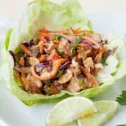 thai chicken lettuce wrap on a plate with lime wedges on the side
