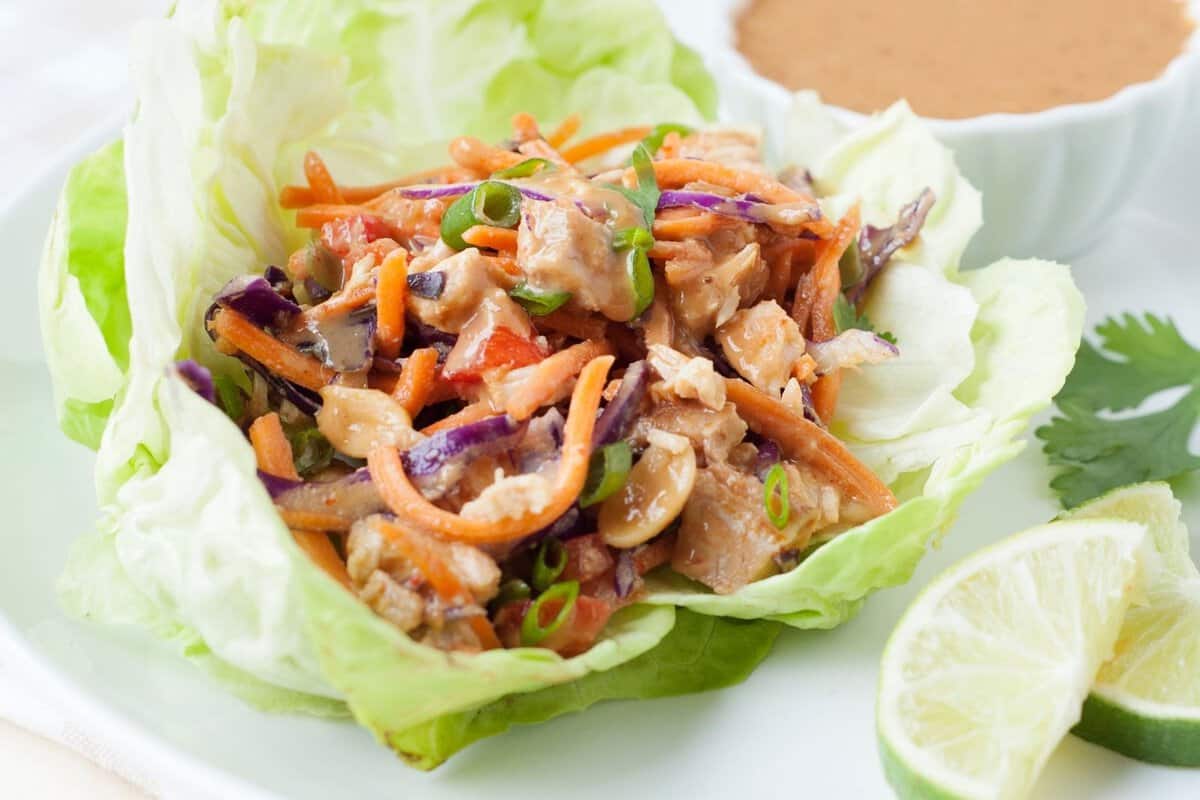 thai chicken lettuce wrap on a plate with lime wedges and peanut sauce on the side
