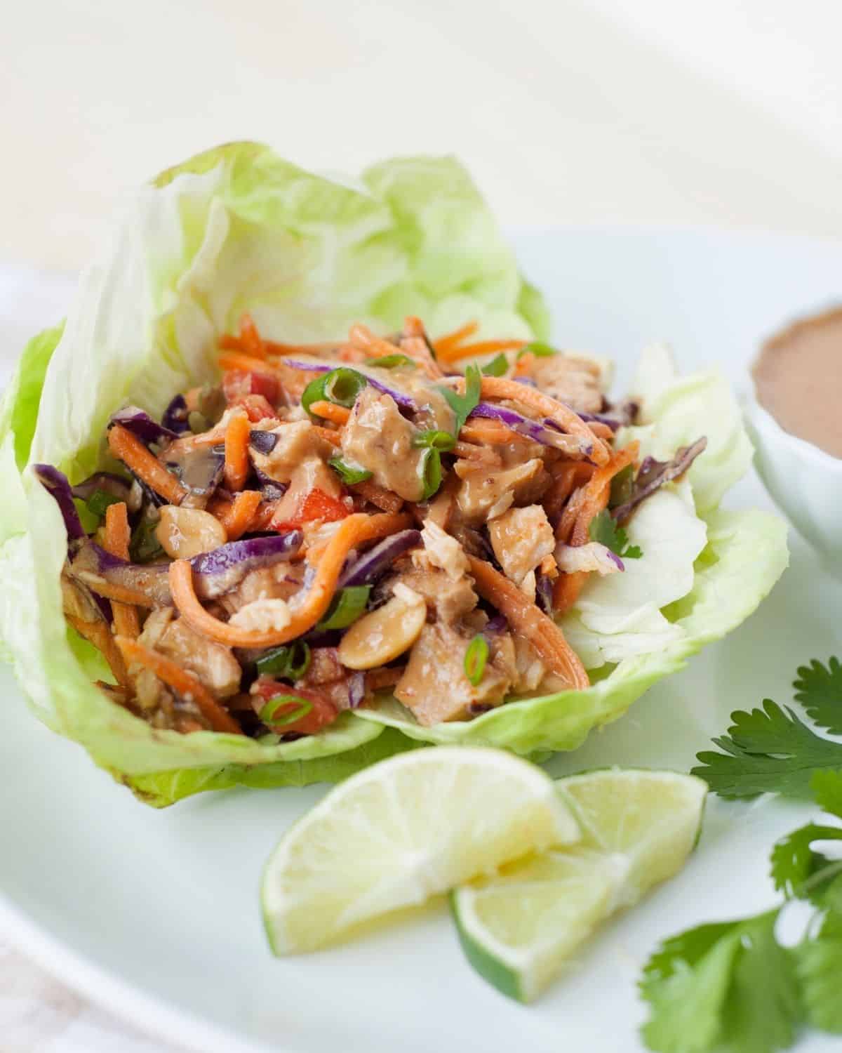 thai chicken lettuce wrap on a plate with lime wedges and peanut sauce on the side