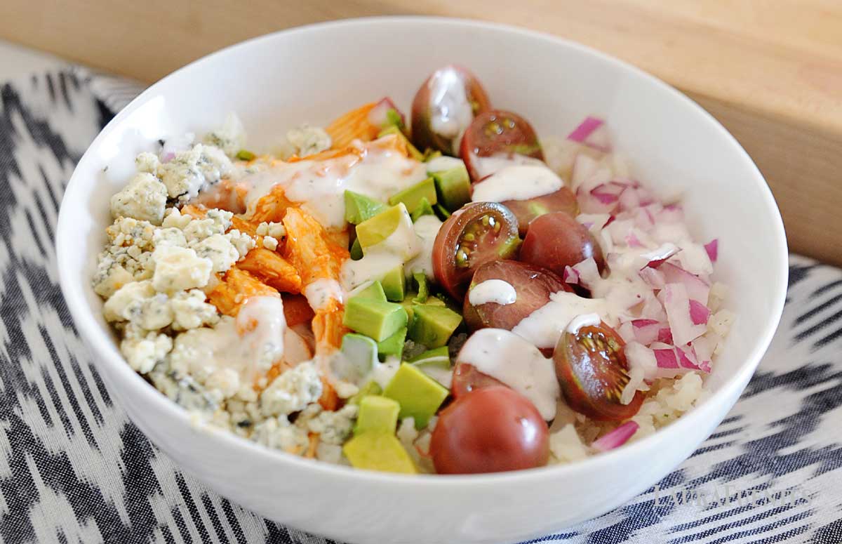 a white bowls of buffalo chicken, rice and vegetables
