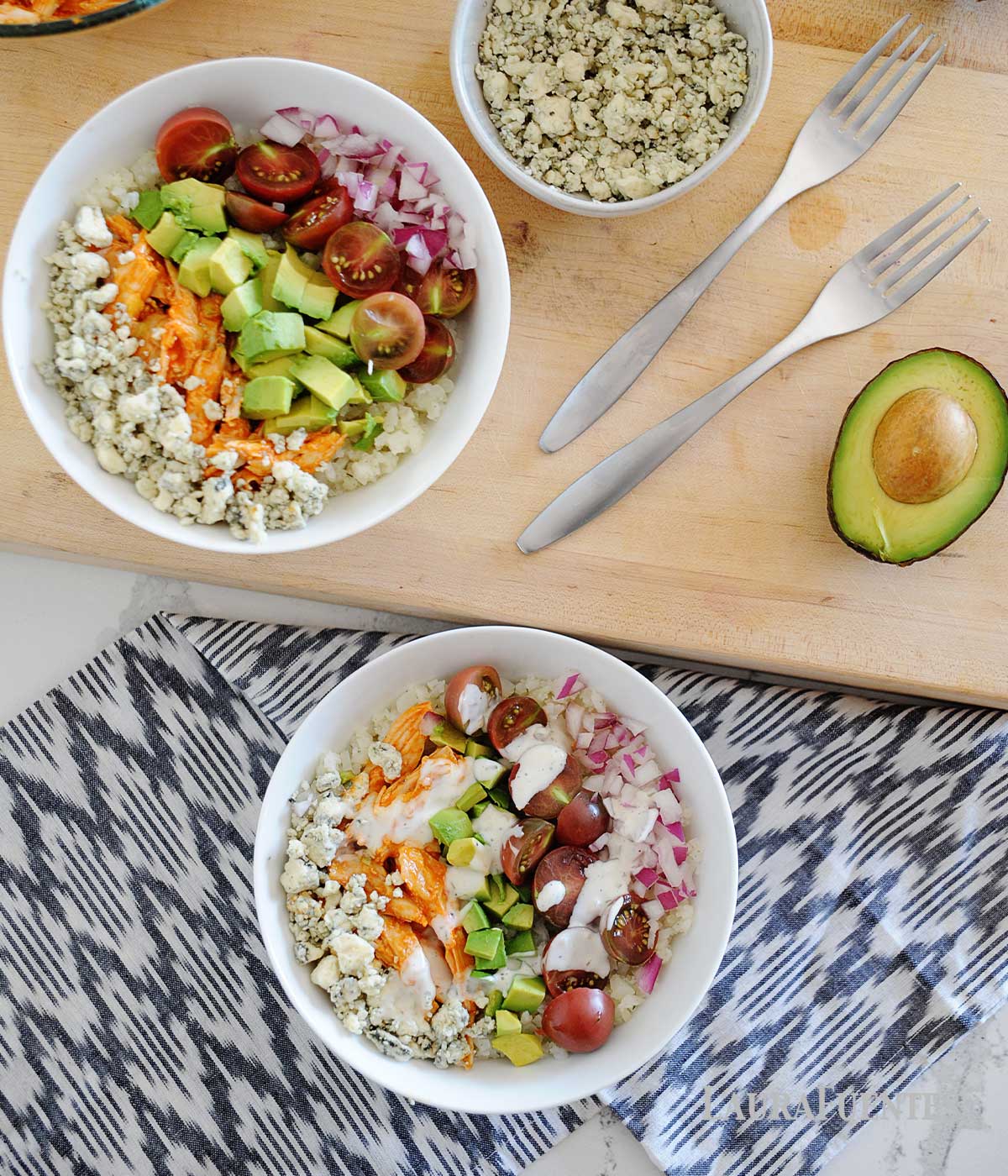 two white bowls of buffalo chicken, rice and vegetables. Bowls of ingredients like chicken and cheese to the side
