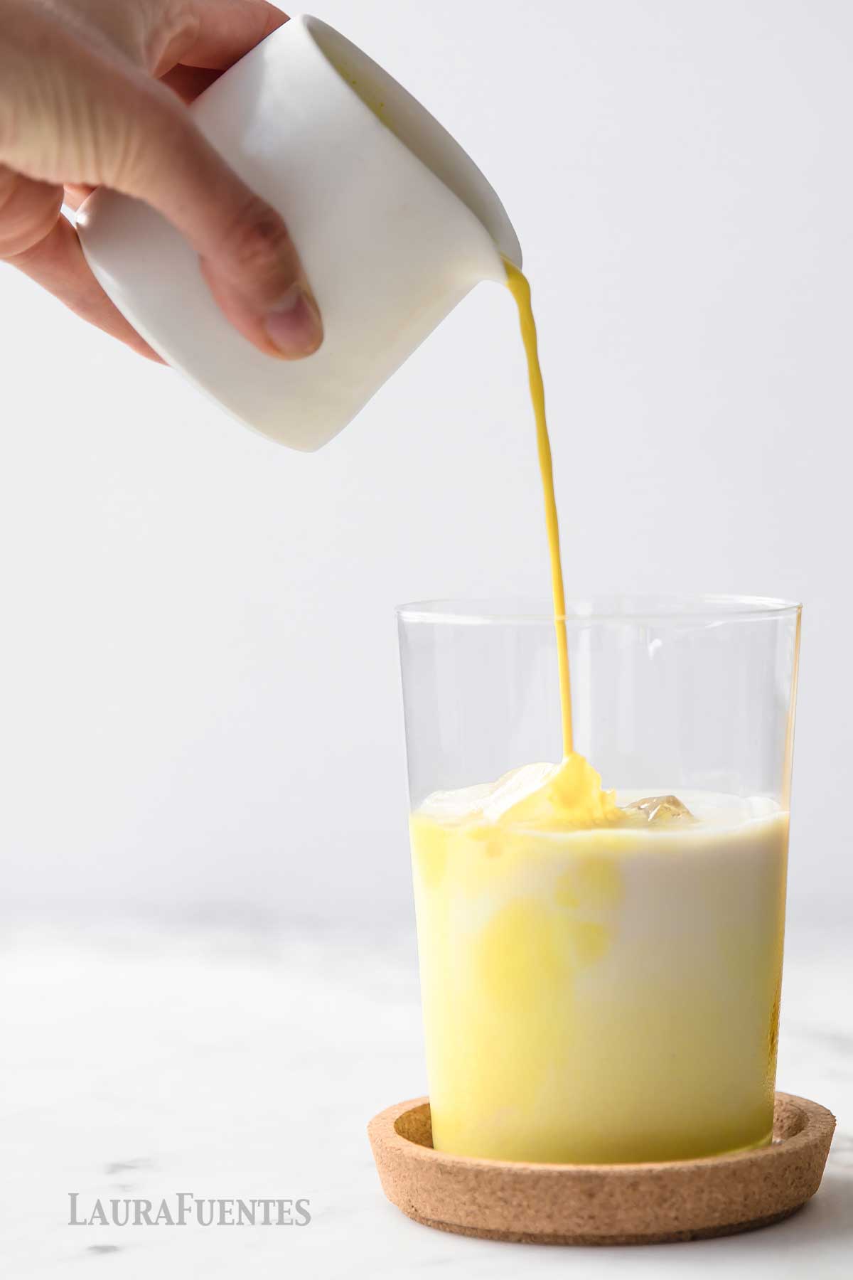 Pouring tumeric mixture into glass of ice milk