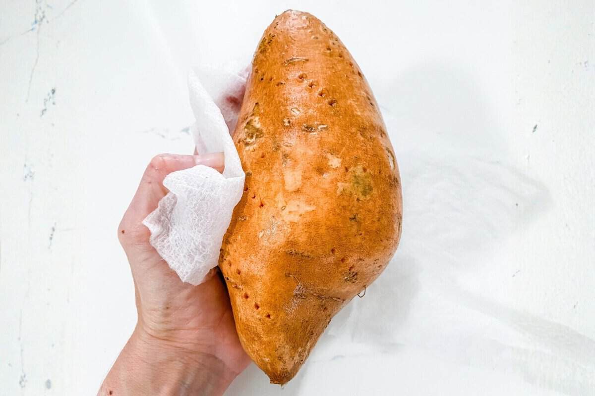 a hand holding a sweet potato with a kitchen towel