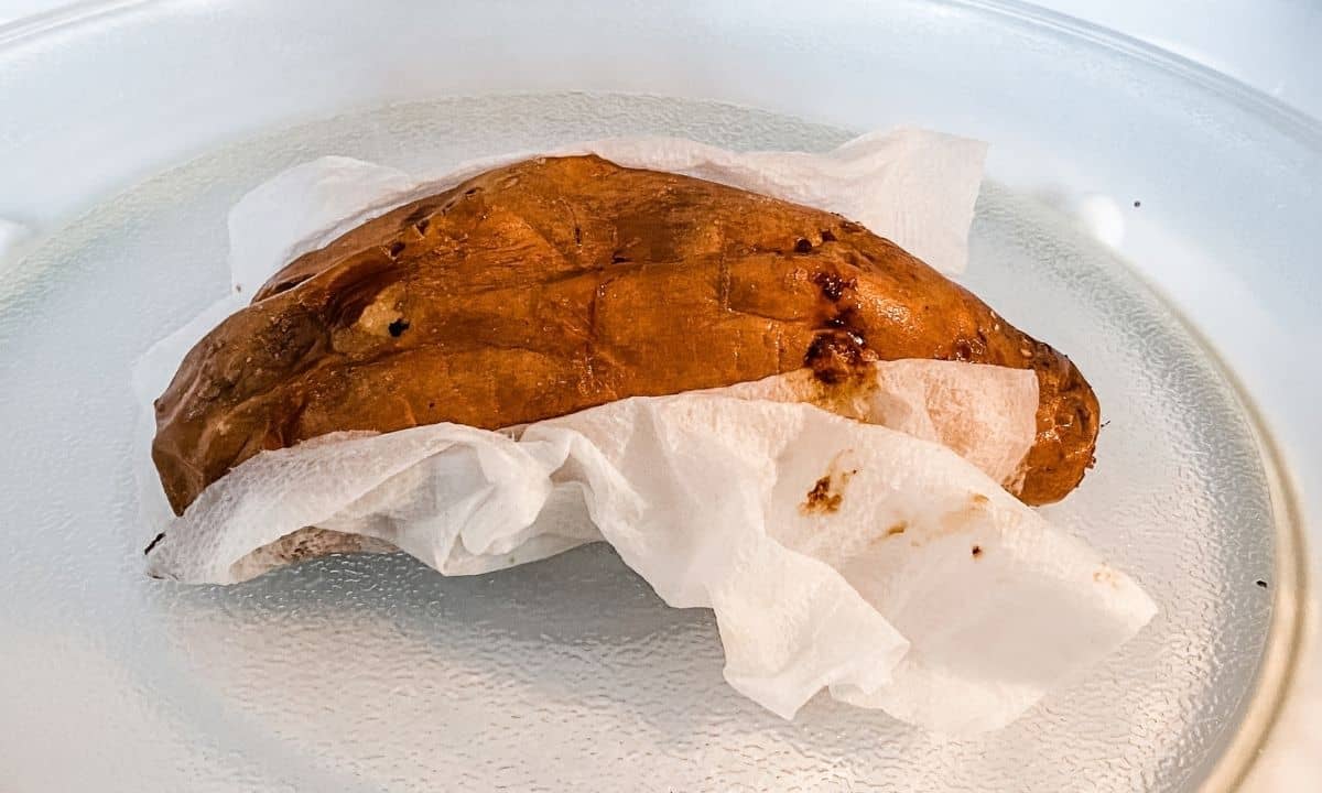 a cooked sweet potato wrapped with paper towel in the microwave