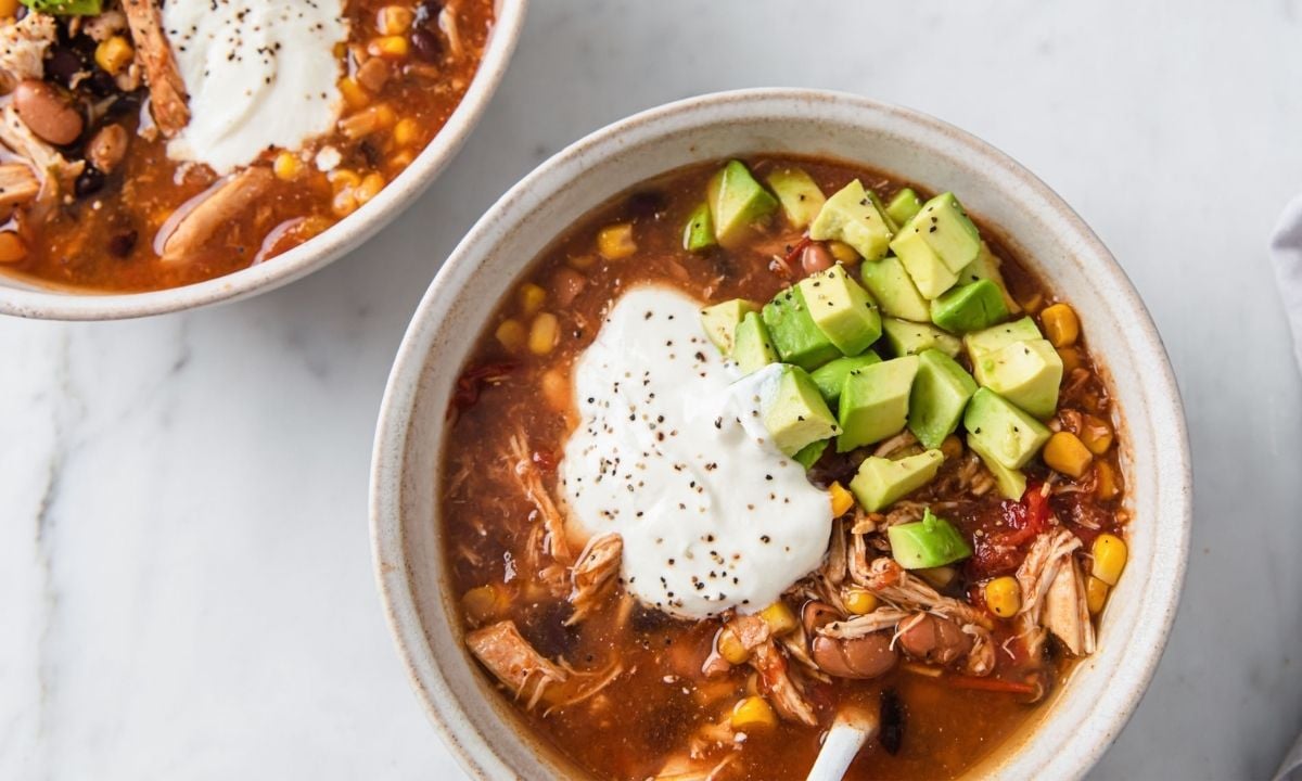 top view of two bowls of chicken taco soup topped sour cream and avocado