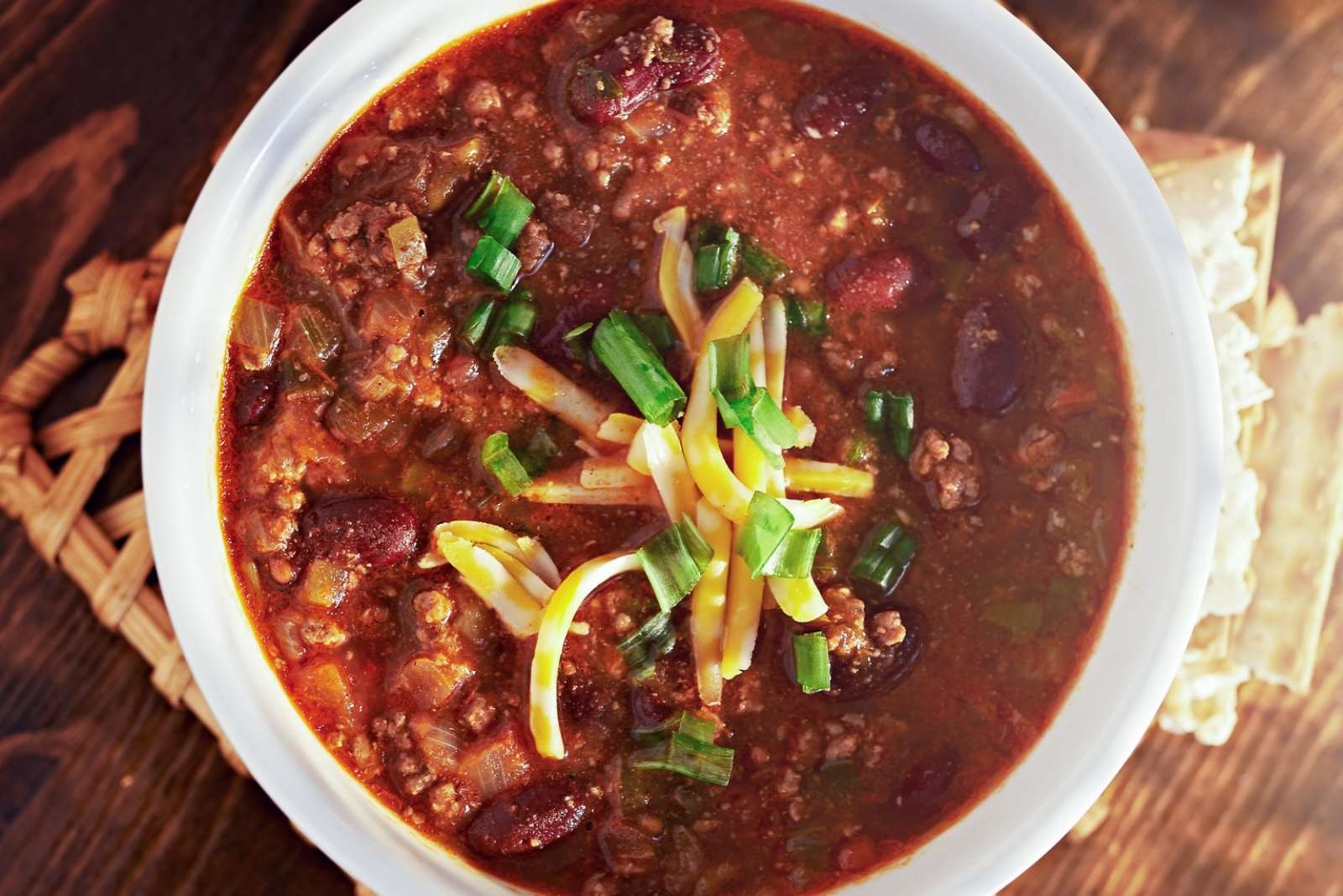 top view of a bowl of ground turkey chili with shredded cheese and chopped green onions