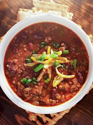 top view of a bowl of ground turkey chili with shredded cheese and chopped green onions