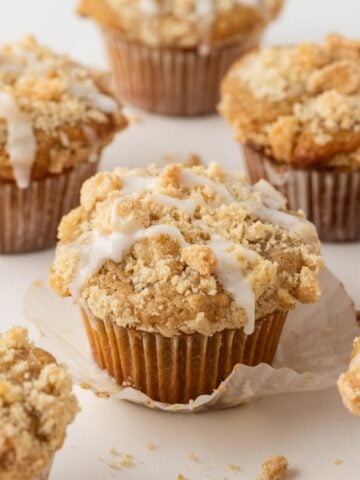 front view of a baked and glazed coffee cake muffin with a cinnamon streusel topping with other muffins in background