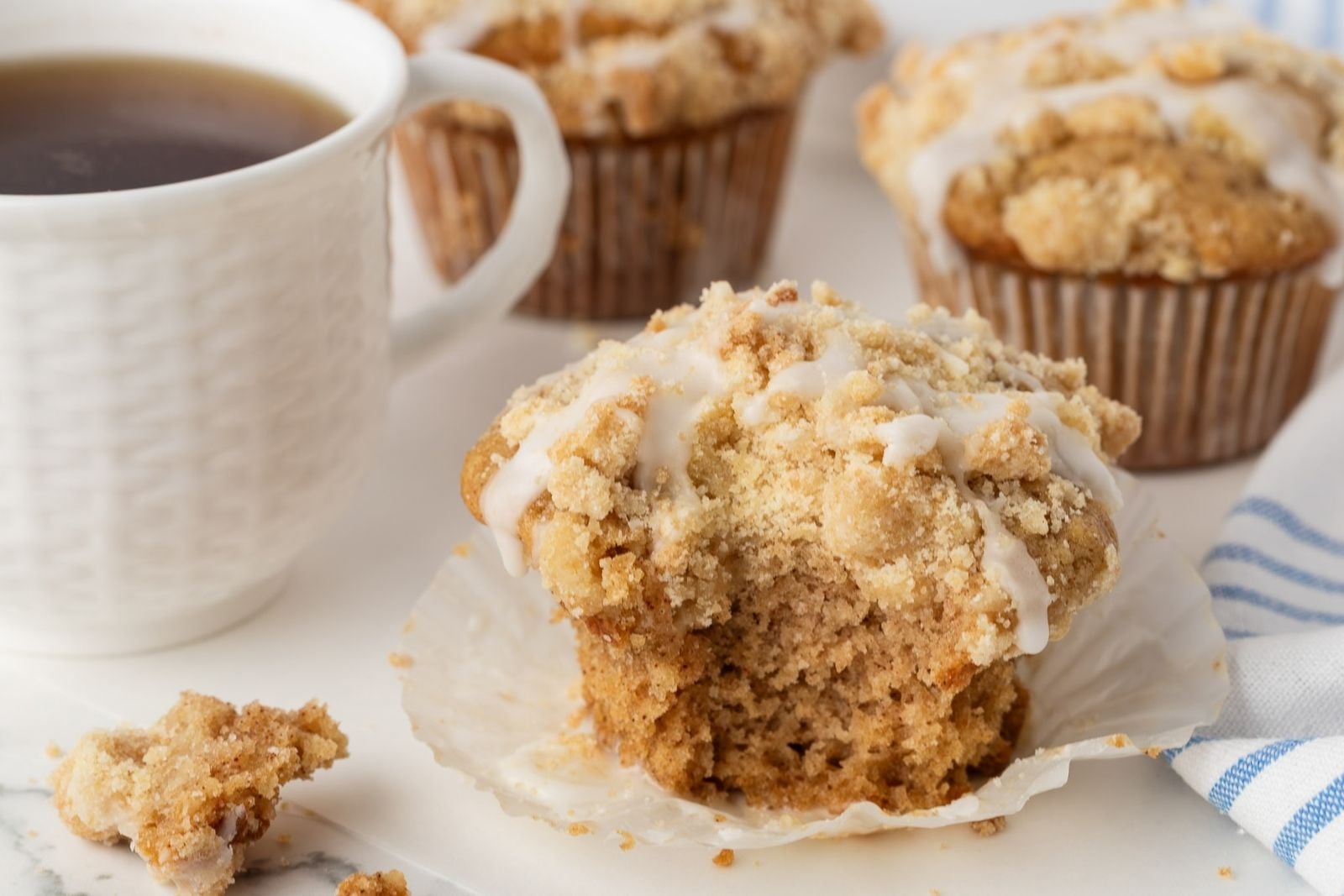 front view of a baked and glazed coffee cake muffin with a cinnamon streusel topping with a bite missing to show the soft and moist inside texture
