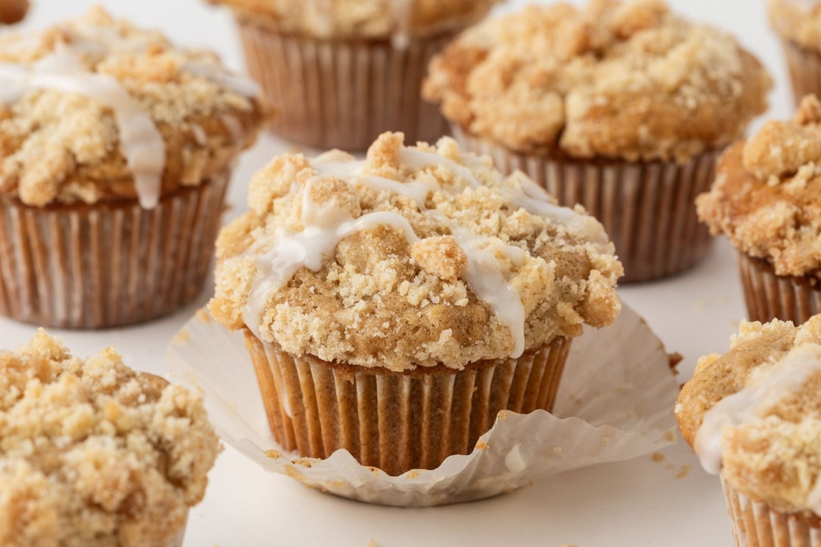 front view of a baked and glazed coffee cake muffin with a cinnamon streusel topping with other muffins in background