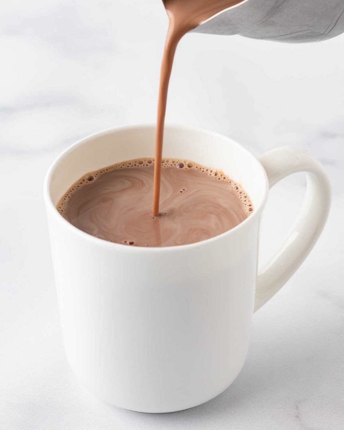 pouring homemade hot cocoa into a mug, showing the color of the rich hot chocolate