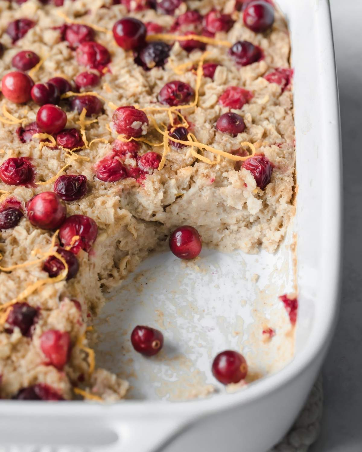 Dish of baked oatmeal with whole cranberries on top, one portion has been cut out of dish.