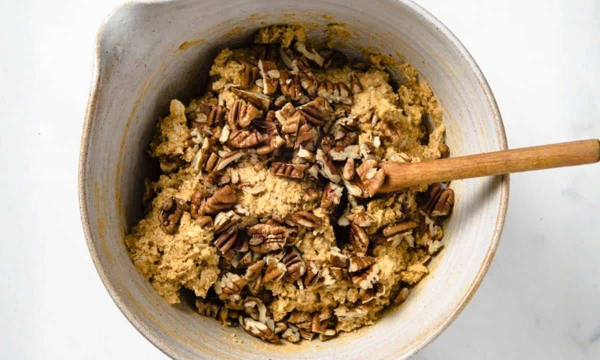 a bowl of wet and dry ingredients being mixed into pumpkin cookie dough