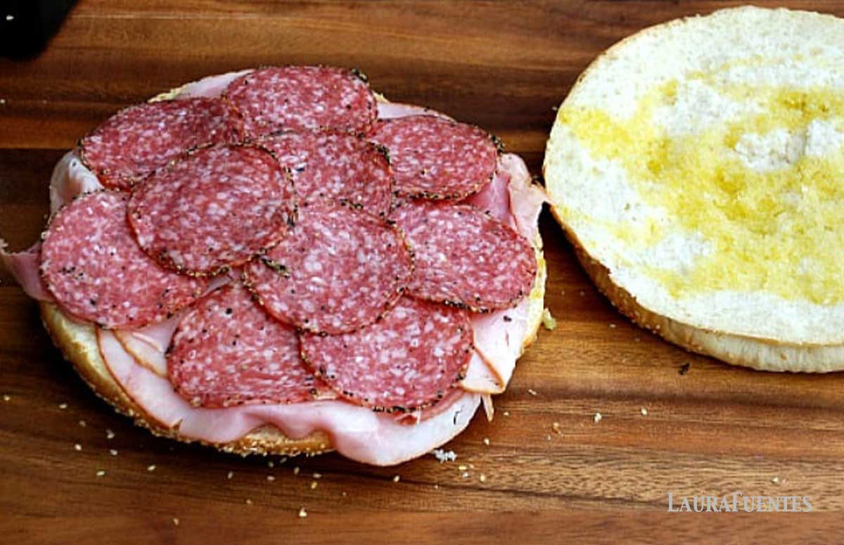 salami and other meats spread out on round muffuletta bread