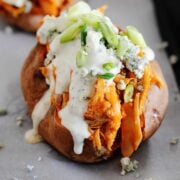 baked sweet potatoes on cooking sheet loaded with buffalo chicken, ranch dressing, green onions and blue cheese crumbles