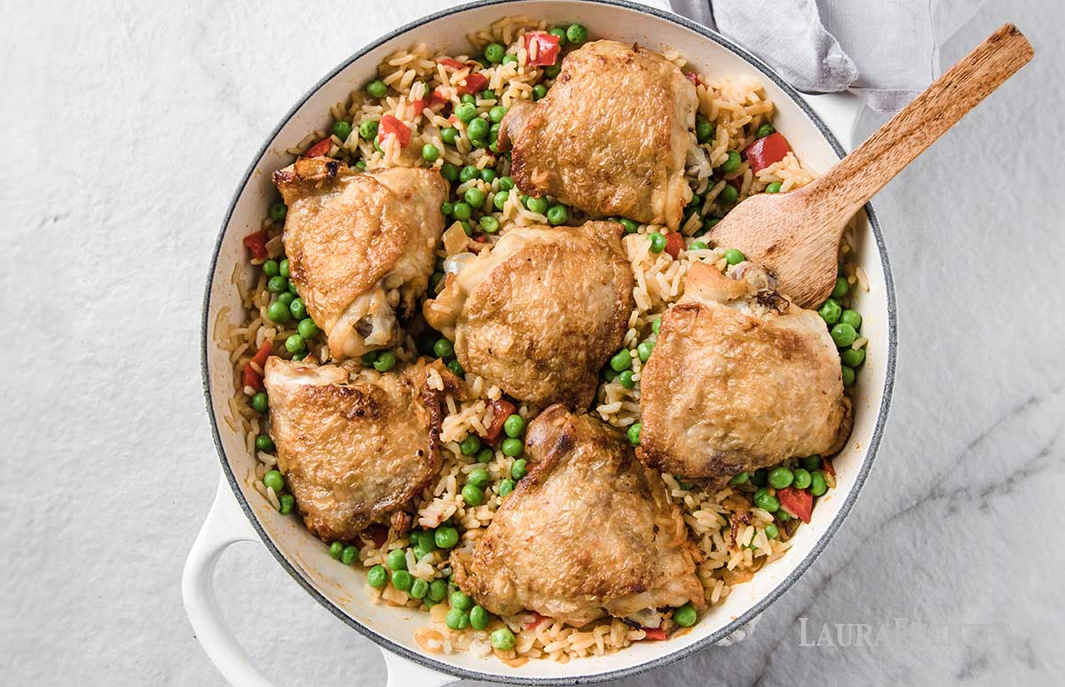 full skillet of rice, peas, peppers and six cooked chicken breasts with crispy skins