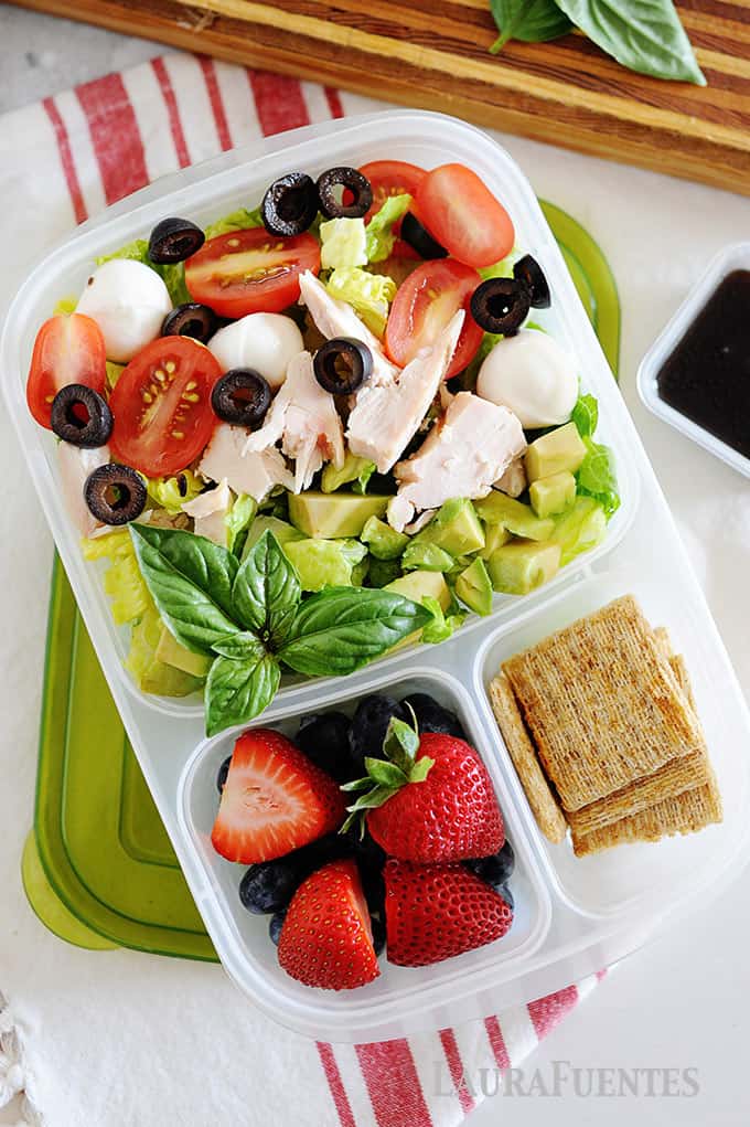 image: chicken caprese sald in a lunch container with berries and crackers
