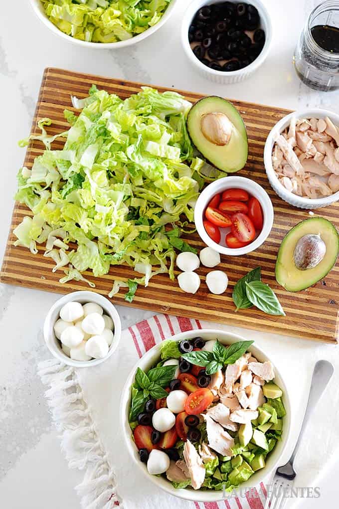 image: bowl of chicken caprese salad with ingredients on a cutting board.