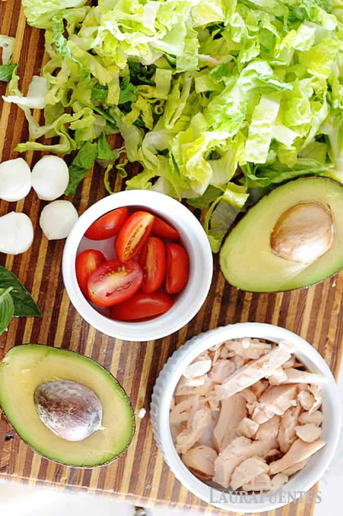 image: ingredients for chicken caprese salad, lettuce, avocados, chicken, cheese and tomatoes