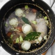 top view of a large pot with chicken, onion, bay leaves, carrots to make broth