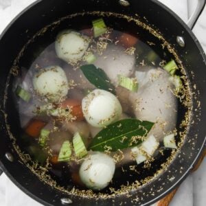 top view of a large pot with chicken, onion, bay leaves, carrots to make broth