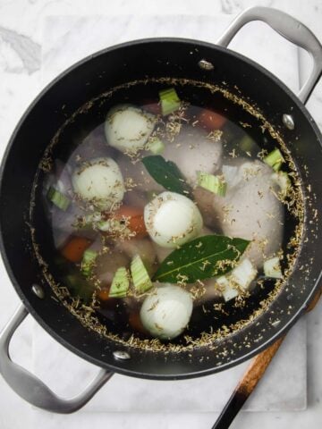 top view of a large pot with chicken, onion, bay leaves, carrots to make broth