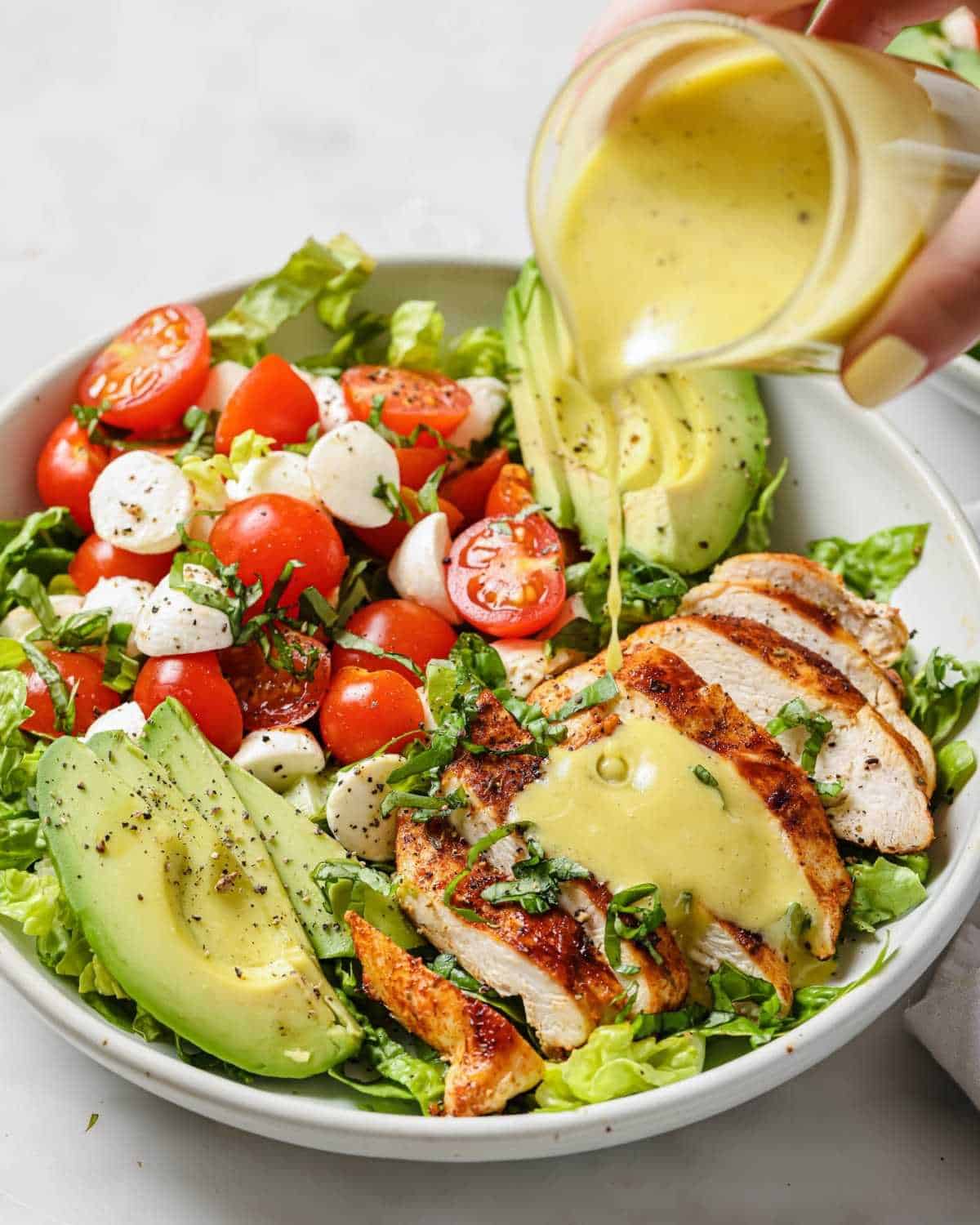 creamy dressing being pour over a chicken caprese salad