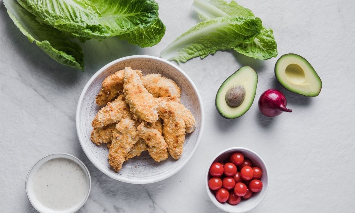 bowls with chicken tenders, dressing, tomatoes, plus lettuce, red onion and avocado