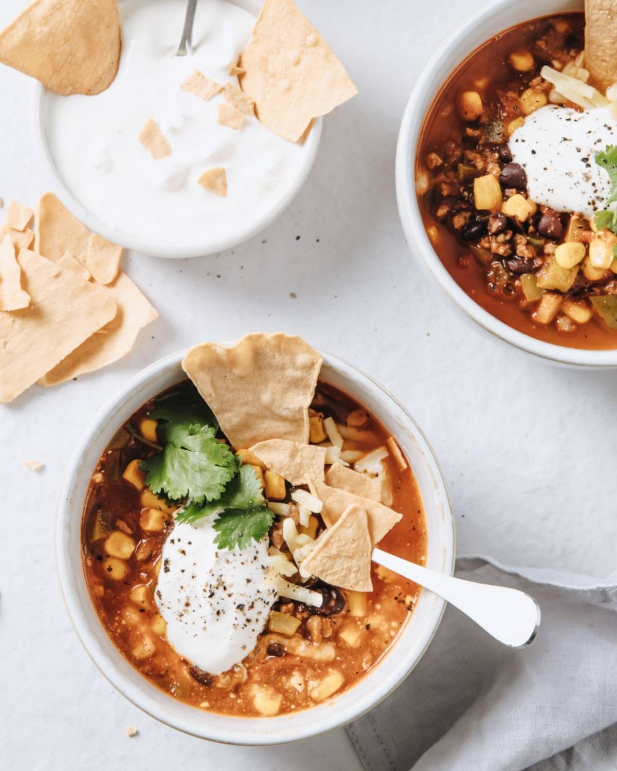 two bowls of taco soup next to a bowl with sour cream and tortilla chips