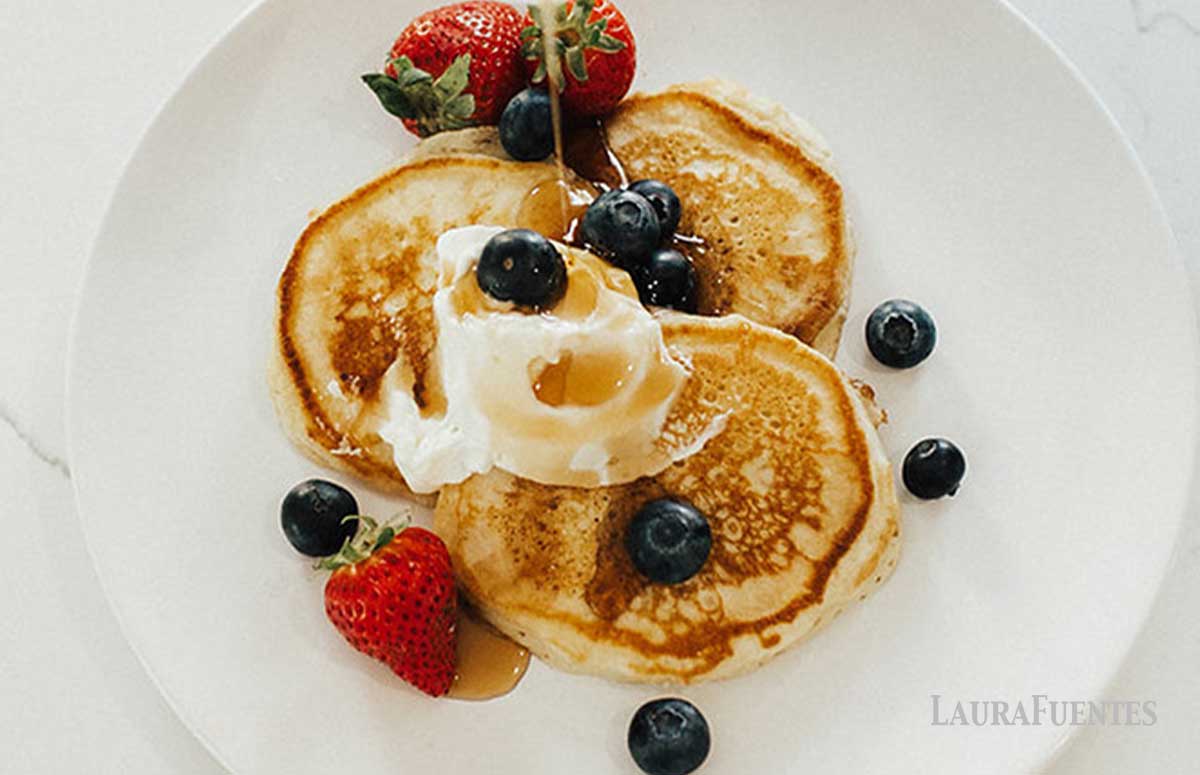image: overhead shot of three small pancakes on a plate top with berries, syrup and whipped cream
